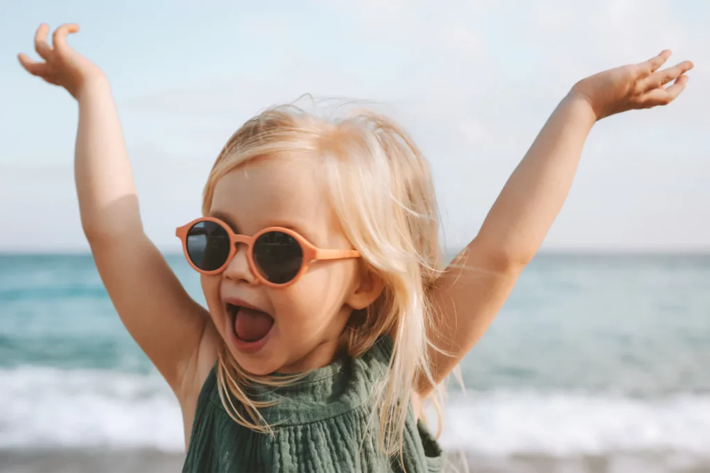 taming your wild child little girl with her arms up in the air and sun glasses