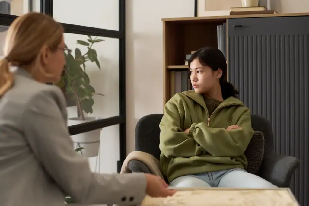 Portrait of angry teenage girl stonewalling therapist during counseling meeting