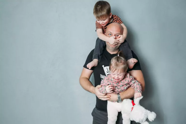 Stressed dad with one little boy on his shoulders and holding his crying toddler he needs a good parenting tool box