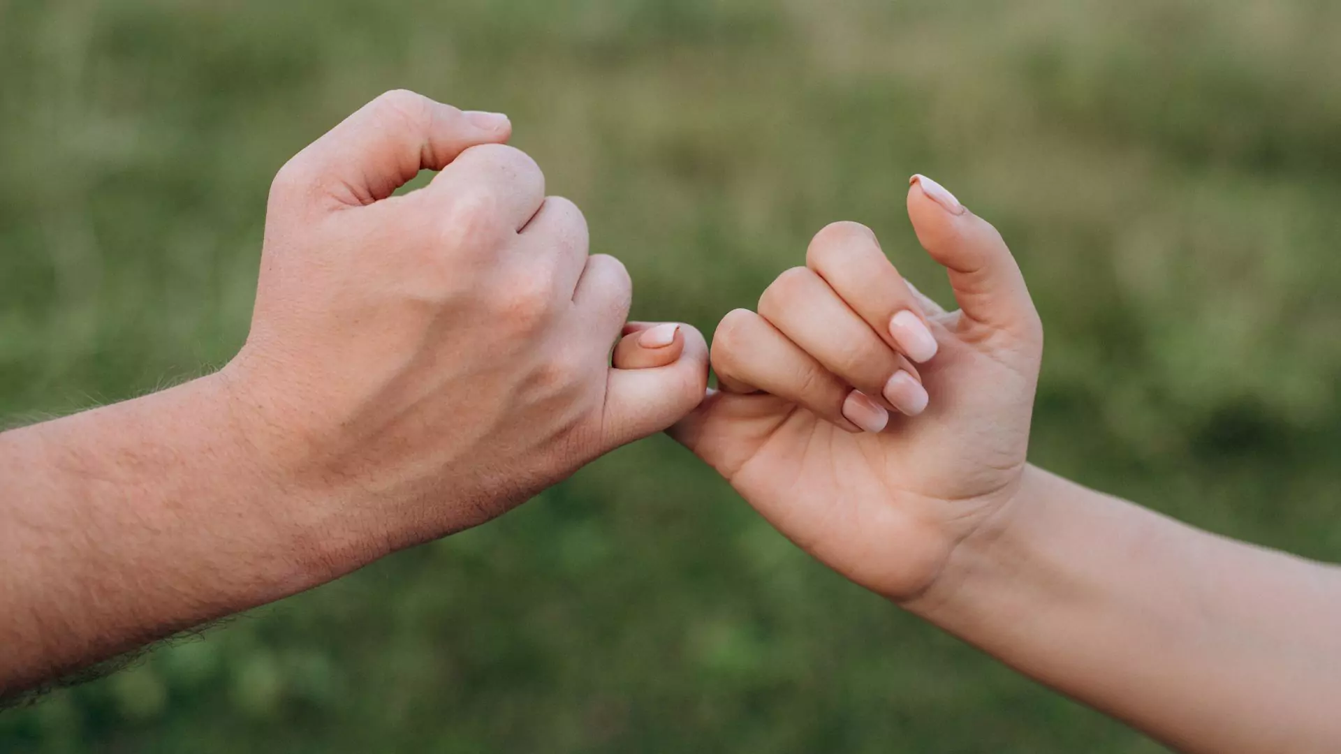 Photo of two hands, a man and woman, with their pinkie fingers interlocked in a promise commitment, symbolizing marriage.