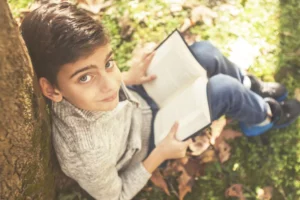 Celebrating Lent by taking a walk in the woods. Little boy reading the bible sitting under a tree