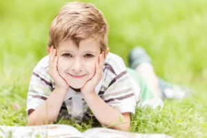 Young boy smiling as he reads Clubhouse magazine on the lawn. John 7:11