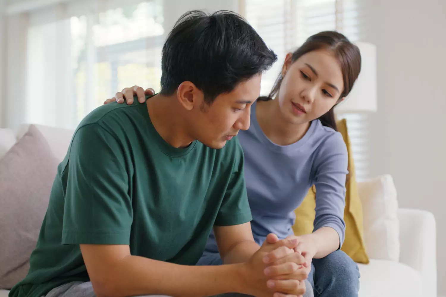 A young couple sits on the couch, with the woman putting an understanding arm on the man's shoulder.