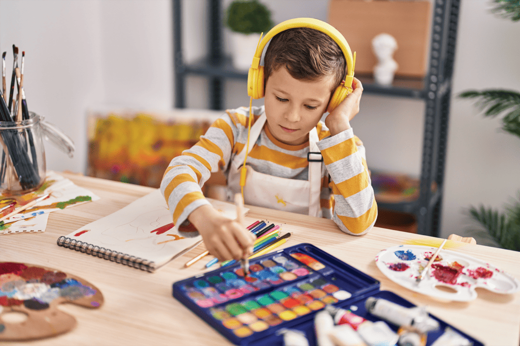 Image of boy wearing headphones while painting at the table.