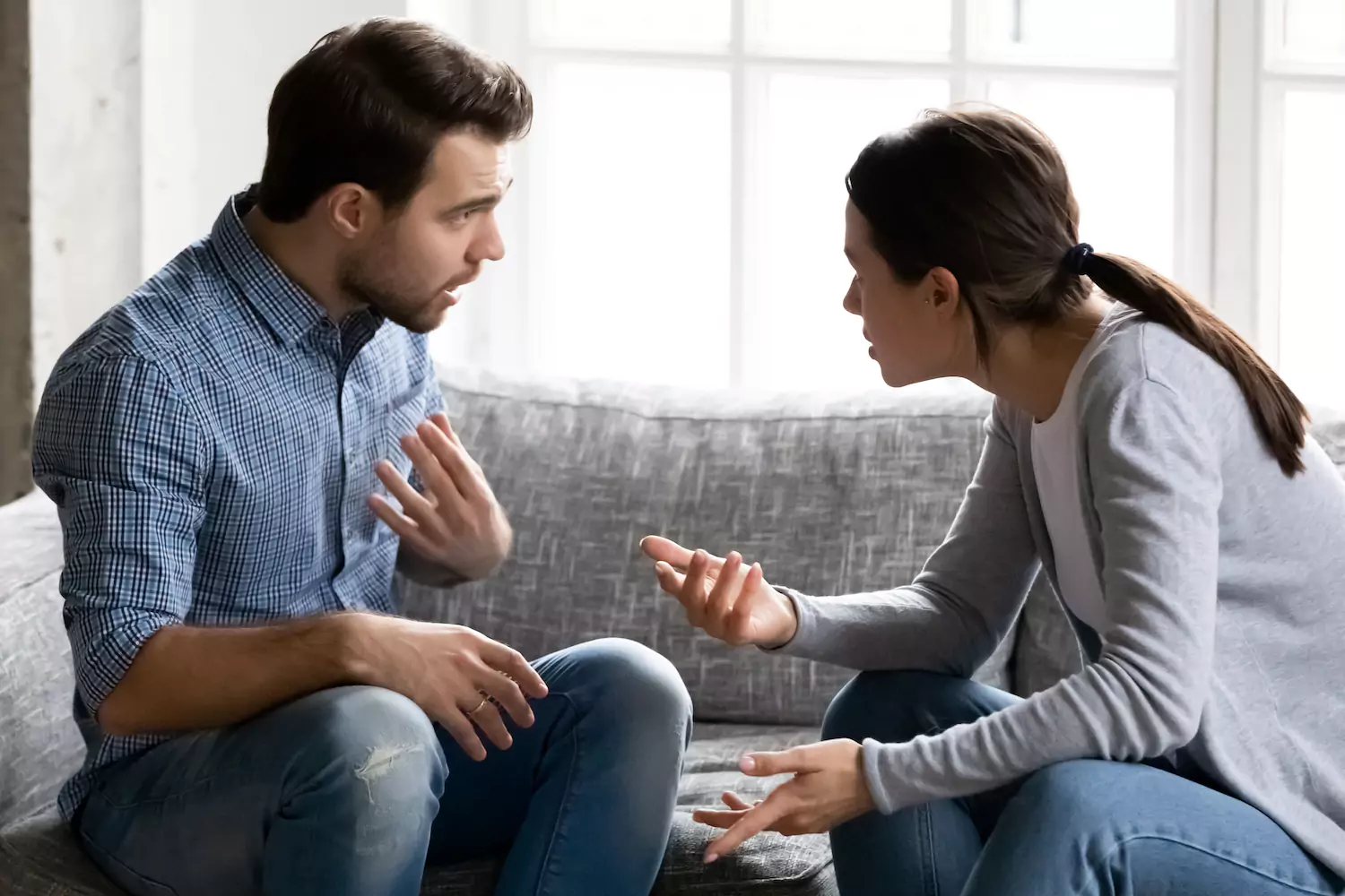 Photo of a married couple talking to eahc other on the couch as a model of communication and conflict in marriagel