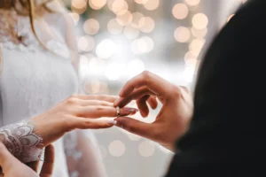 A close-up of a bride and a groom at the wedding, with the groom putting the wedding ring on the bride's finger.