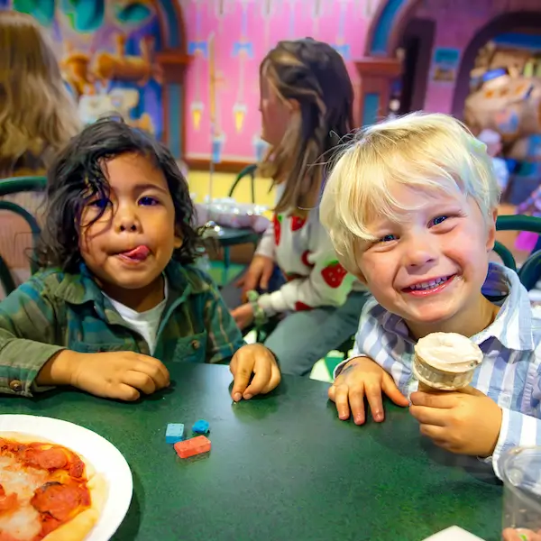 Two young boys eating pizza and ice cream smiling at the camera