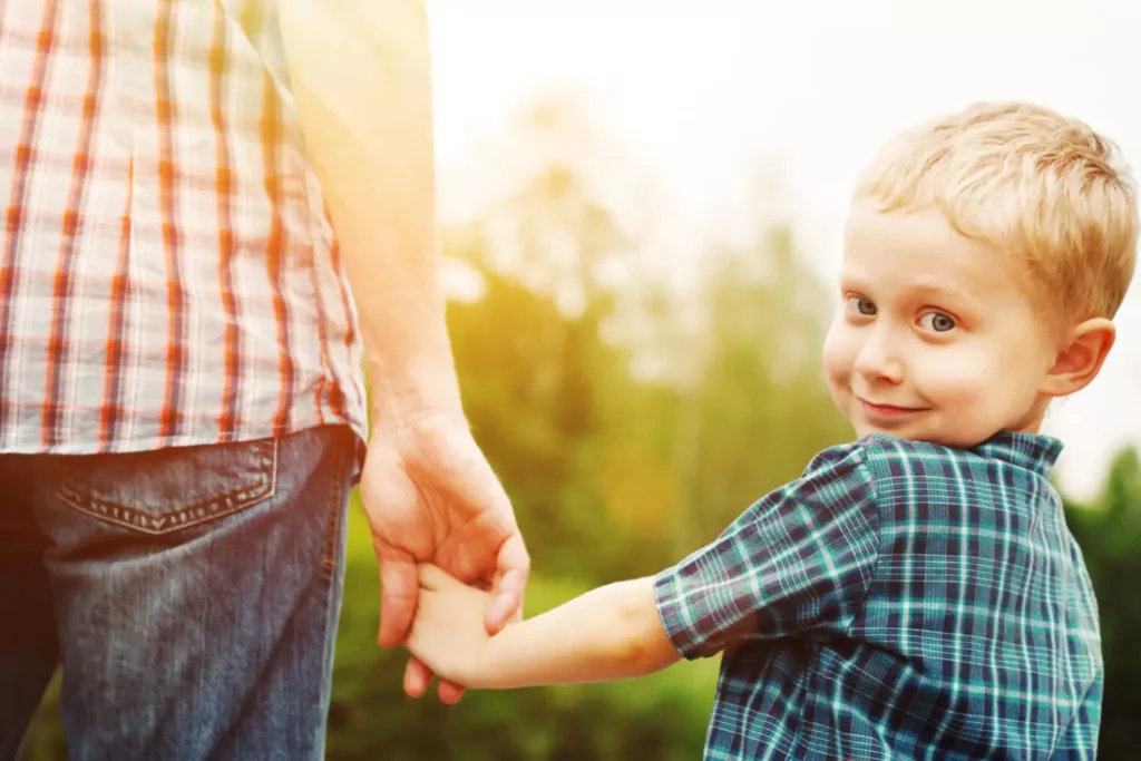 The impact of radical feminism on boys and men. Little boy looking back and smiling as he is holding his daddy's hand