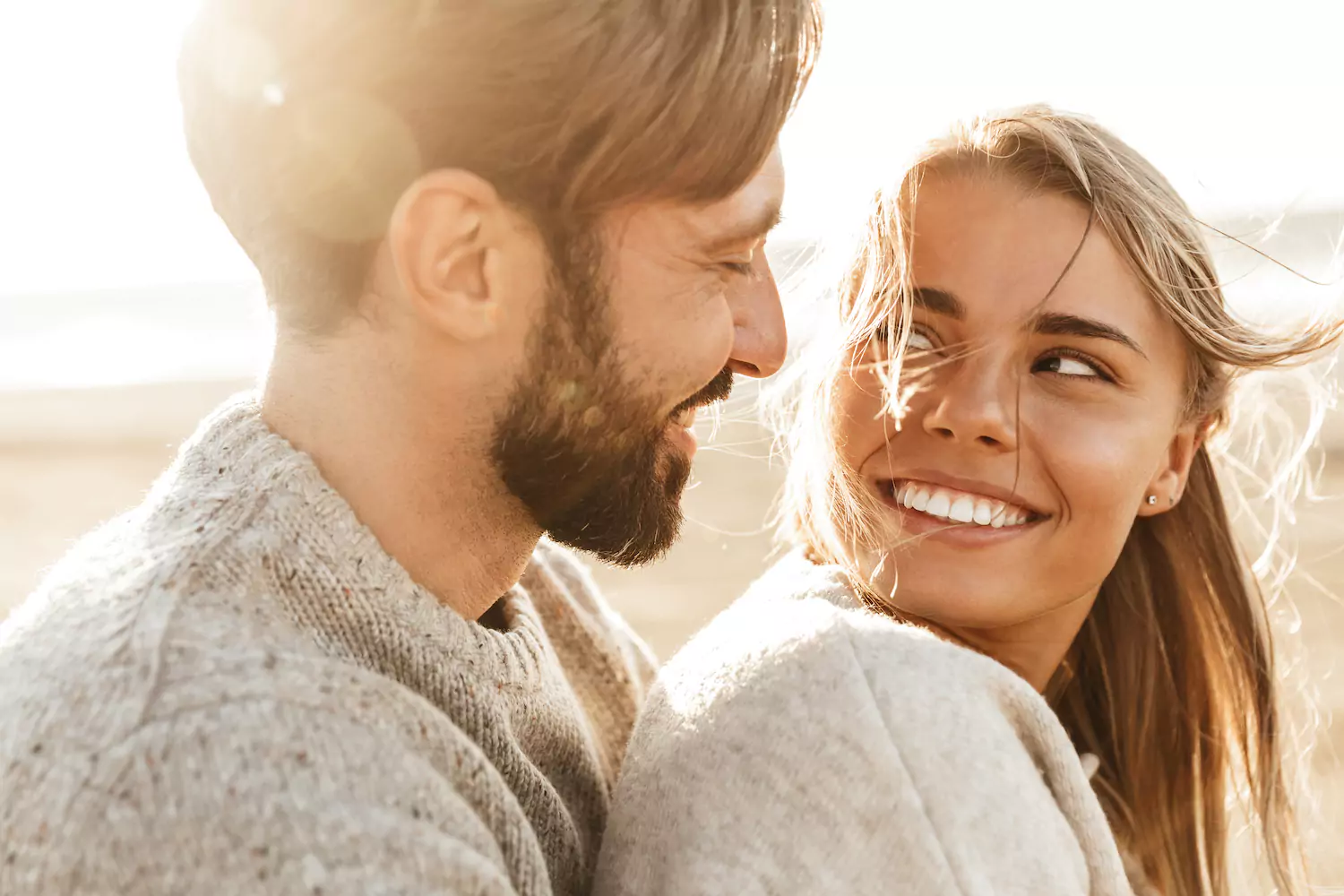 A young couple sit close together in the sun, gazing into each other's eyes.