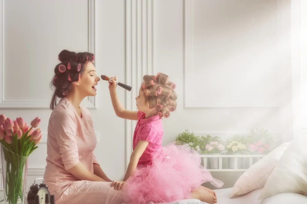 Celebrating Mother's Day With Young Children mom and little girl sitting on a bed with curlers in their hair playing in makeup