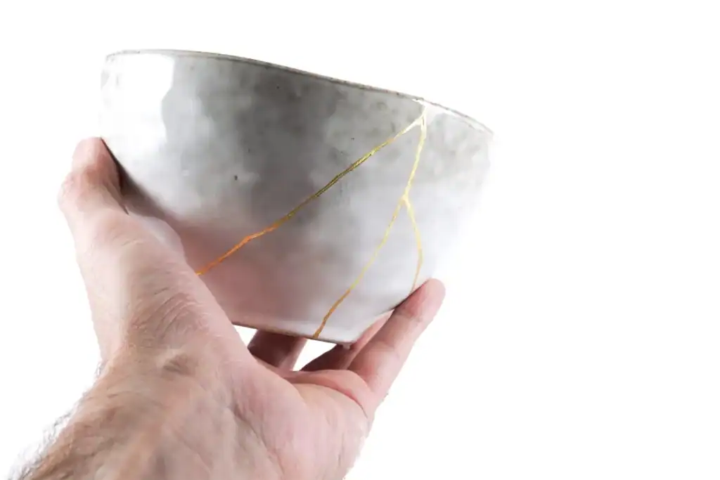 A hand holds a ceramic bowl repaired with visible gold-filled cracks, illustrating the concept of restoration and the theme “God Restores.”