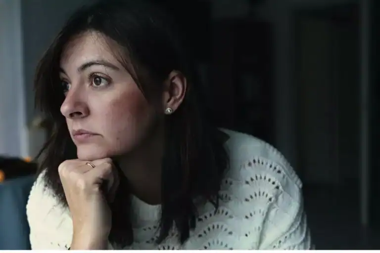 A woman sits indoors wearing a light knit sweater, resting their head on a hand, illustrating a reflective moment connected to the theme of turning your child over to God.