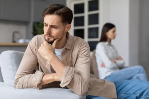 A man and a woman sit on opposite ends of a couch, turned away from each other. Here's how to identify and deal with a spouse on the autism spectrum, and to navigate autism and marriage.