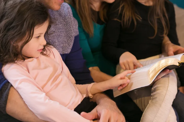 Faith Development and Homeschooling little girl sitting on her mom's lap as a bible is being read to her