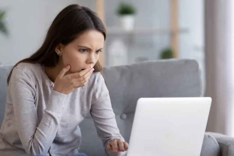 Shocked young woman looking at her laptop, her hand is over her mouth