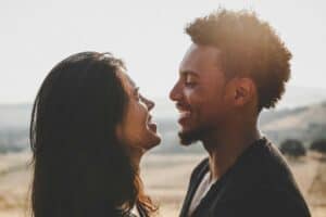 “A couple smiles warmly at each other, standing close together with mountains in the background, capturing a moment of keeping the romance alive.”