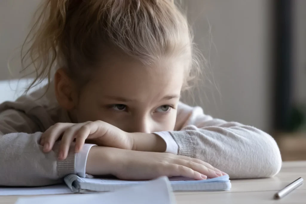 School-age girl at the table resting her arms on her book and her head on her arms