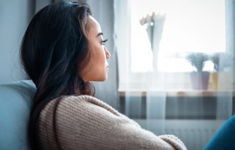 A woman sitting on a couch deep in thought while staring out the window