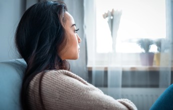 A woman sitting on a couch deep in thought while staring out the window