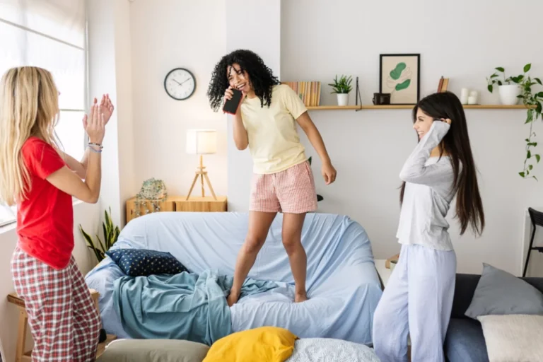 Three young teens in their pajamas, one standing on a couch pretending to sing and dance on stage