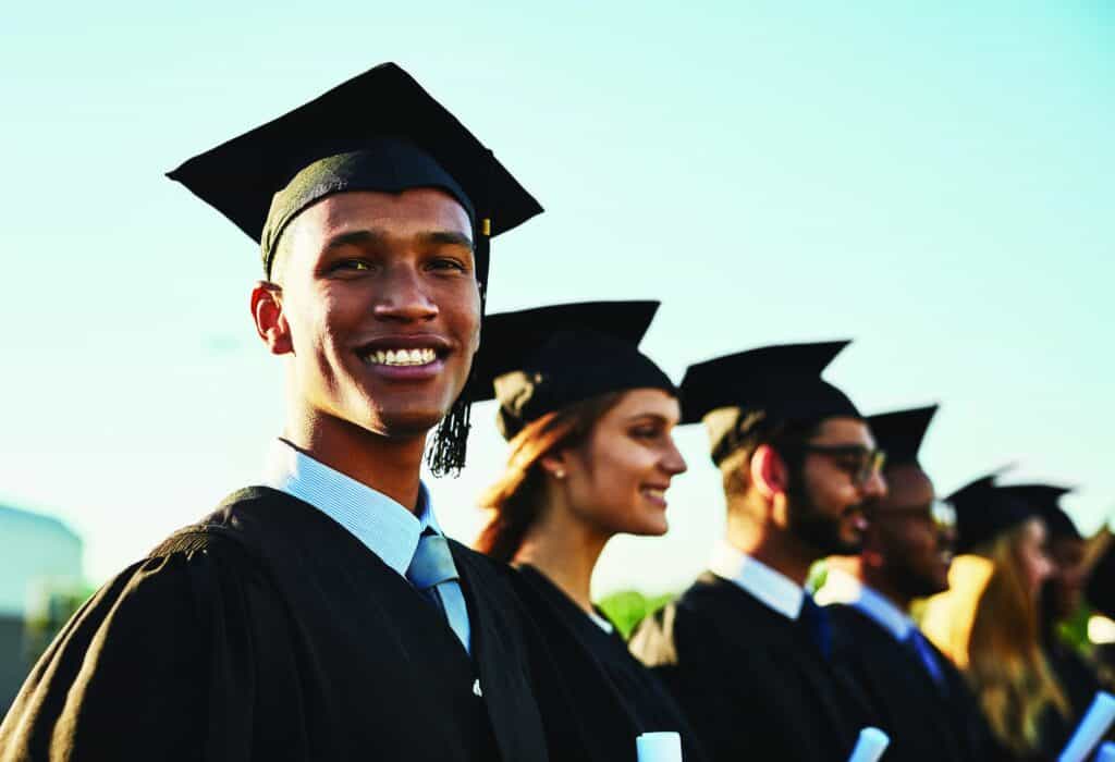 Black man, student smile and graduation ceremony with class group for education, qualification or future. Portrait of happy person and scholar with goals for diploma, certificate or degree on campus