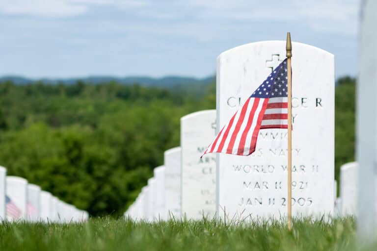American flag stuck in ground in front of white military gravestone memorials in rural cemetery