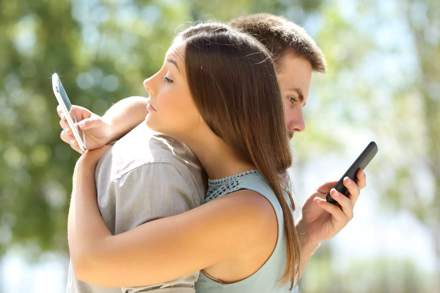 A couple embracing while both are distracted by their phones, highlighting the impact of social media on relationships.