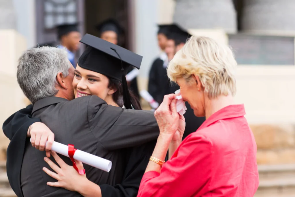 Graduating student hugs father as emotional mother watches, capturing the heart of empty nest syndrome.