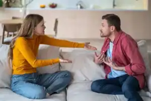 Two adults engaged in a serious discussion while seated on a couch in a living room, illustrating conflict resolution and communication challenges often explored in Bible verses about anger in relationships.