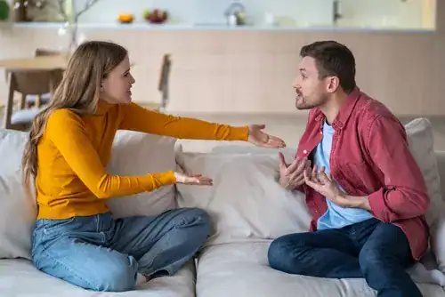 Two adults engaged in a serious discussion while seated on a couch in a living room, illustrating conflict resolution and communication challenges often explored in Bible verses about anger in relationships.