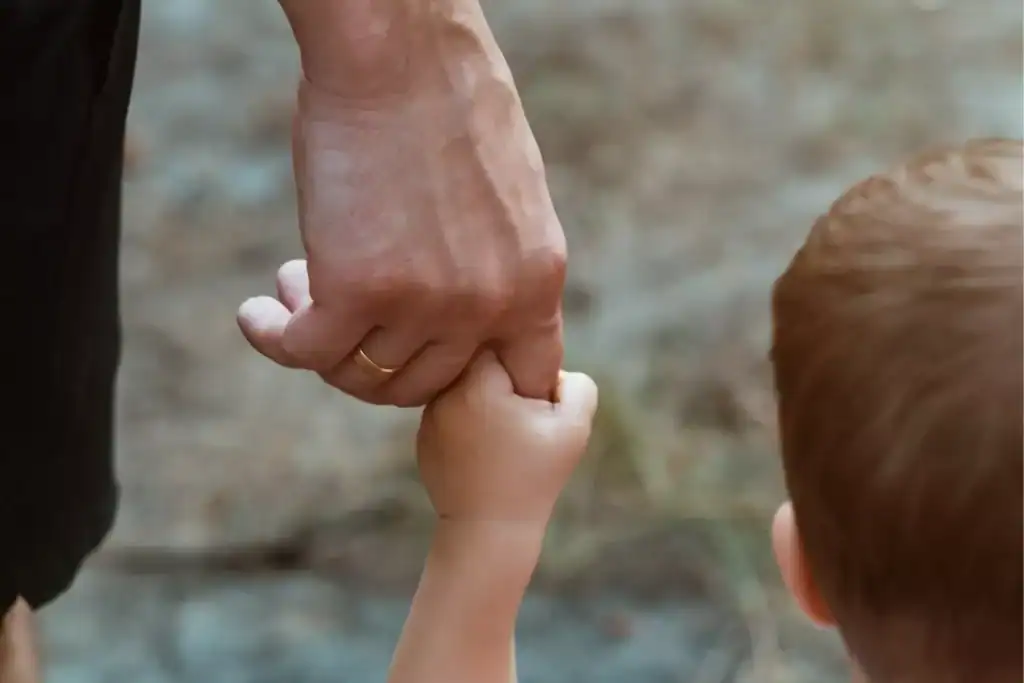 A close-up of an adult hand gently holding a child's hand while walking outdoors, symbolizing the power of gentleness.