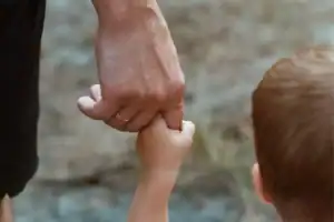 A close-up of an adult hand gently holding a child's hand while walking outdoors, symbolizing the power of gentleness.