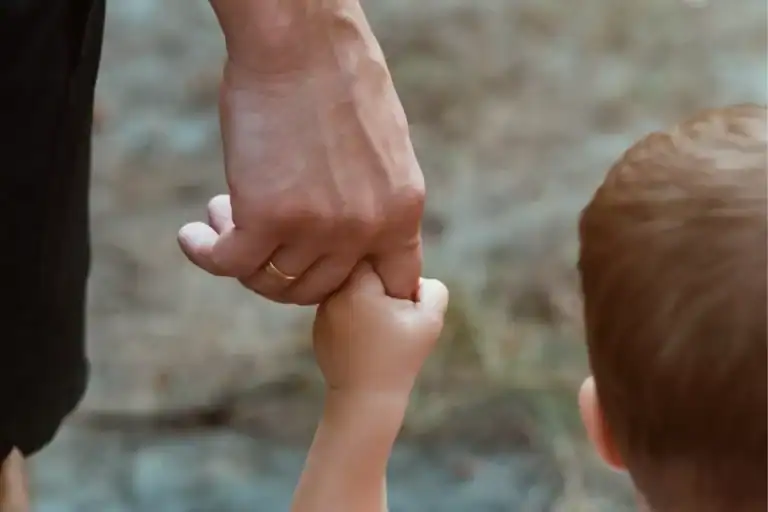 A close-up of an adult hand gently holding a child's hand while walking outdoors, symbolizing the power of gentleness.