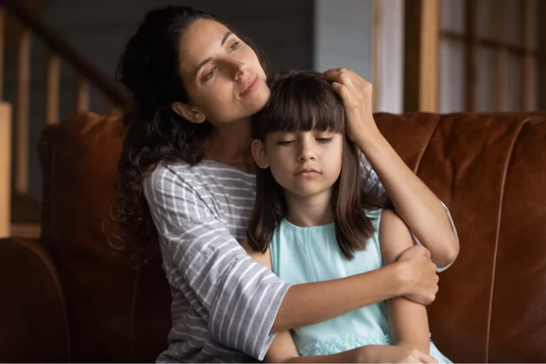 Mother gently hugging her daughter on a couch, both looking thoughtful, symbolizing emotional support in easing visitation for your child after divorce.