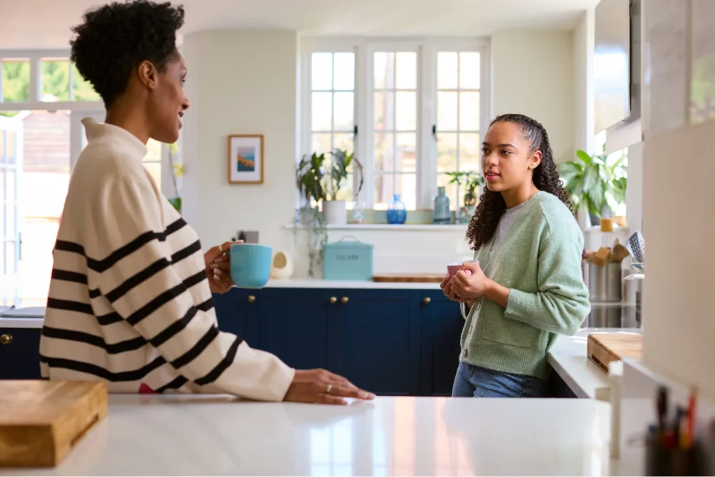 A mother and her teenage daughter having a serious conversation in a bright kitchen, symbolizing a moment of open communication.