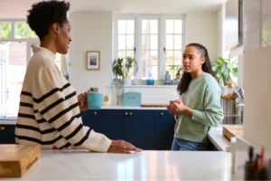 A mother and her teenage daughter having a serious conversation in a bright kitchen, symbolizing a moment of open communication.