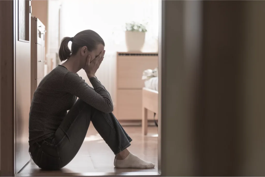A mom feeling guilt with head in her hands sitting on the floor.