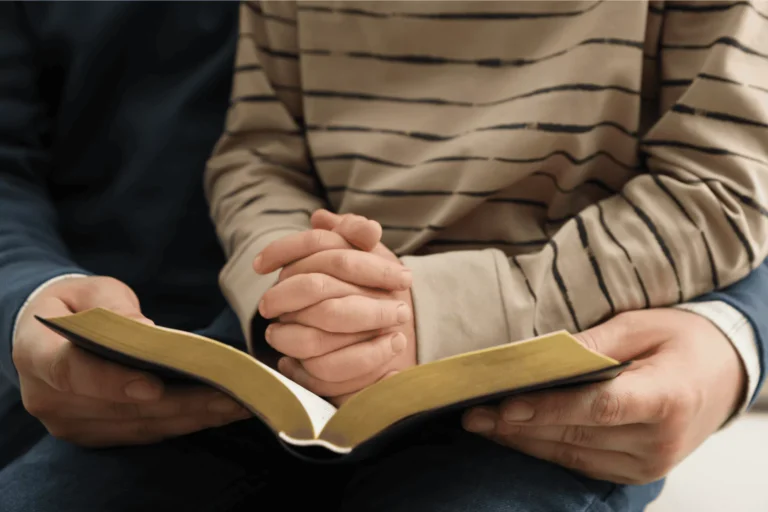 Adult and child reading the Bible together, with the child’s hands folded in prayer – a visual of teaching children biblical truth.