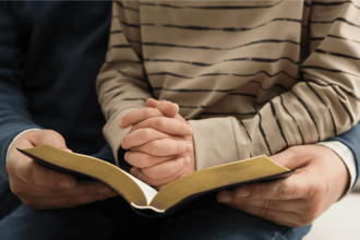 Adult and child reading the Bible together, with the child’s hands folded in prayer – a visual of teaching children biblical truth.