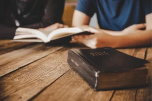 Christian teen with a Bible open on a wood table being discipled by a parent.