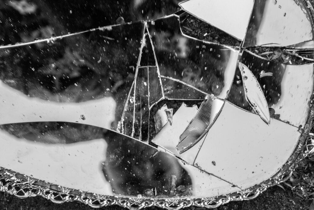 black and white image of a person looking down into a cracked mirror