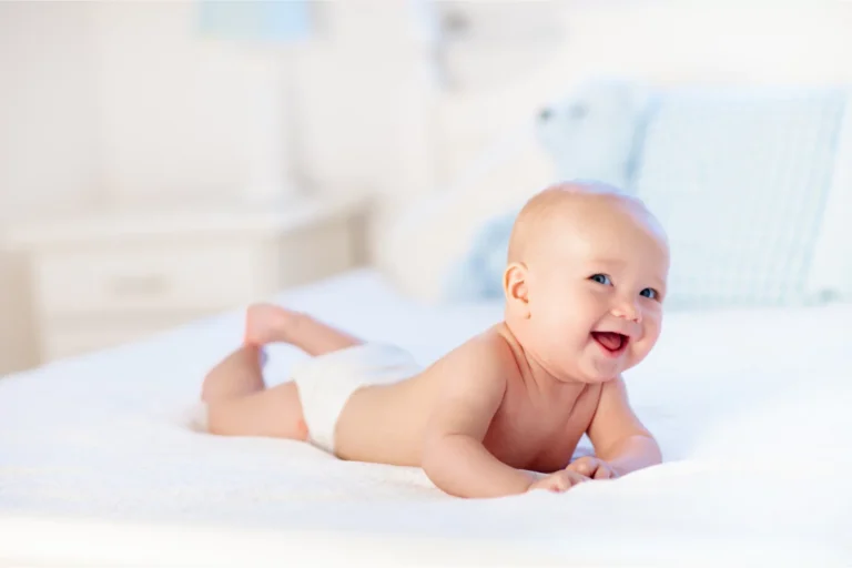 Smiling baby doing tummy time on a bed to build neck strength
