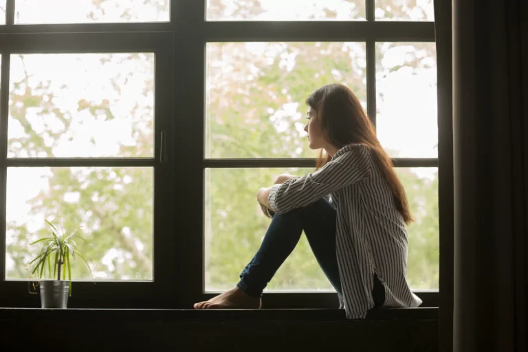 Teen girl sits alone on a windowsill, looking out with a pensive expression, symbolizing the silent struggle behind childhood suicide.