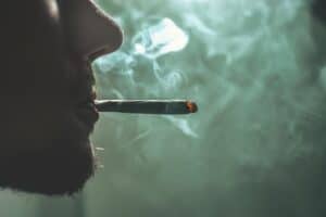 This image shows a person smoking a cigarette. Displayed is a close up of the side profile with the cigarette as the main focus. What Does the Bible Say About Drugs?