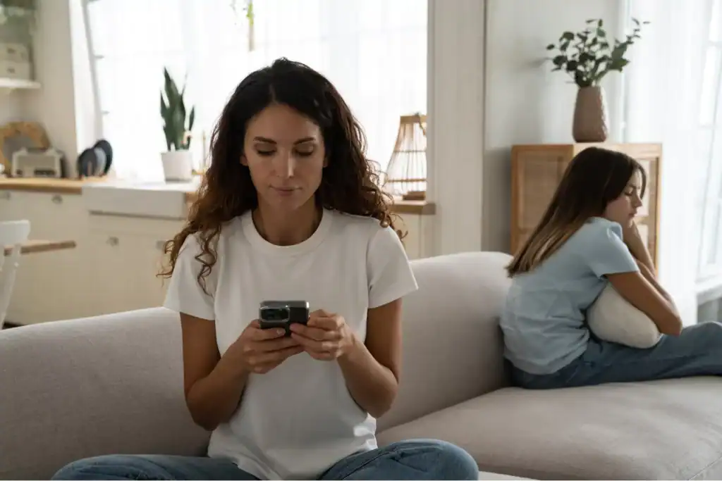 Mother focused on her phone while daughter sits upset beside her, highlighting the importance of taking a break from social media.