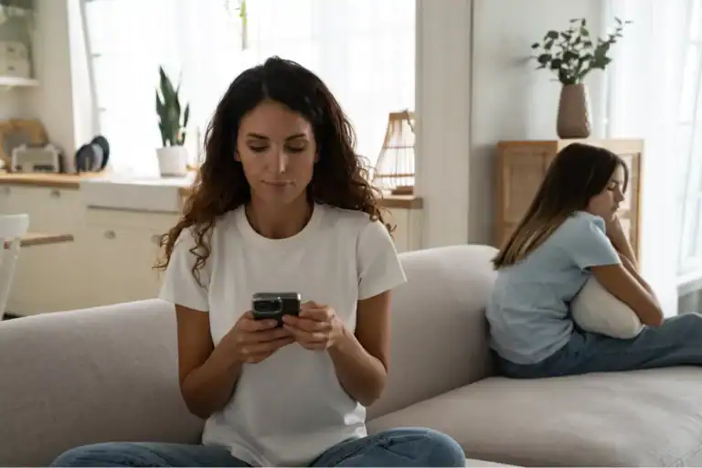 Mother focused on her phone while daughter sits upset beside her, highlighting the importance of taking a break from social media.