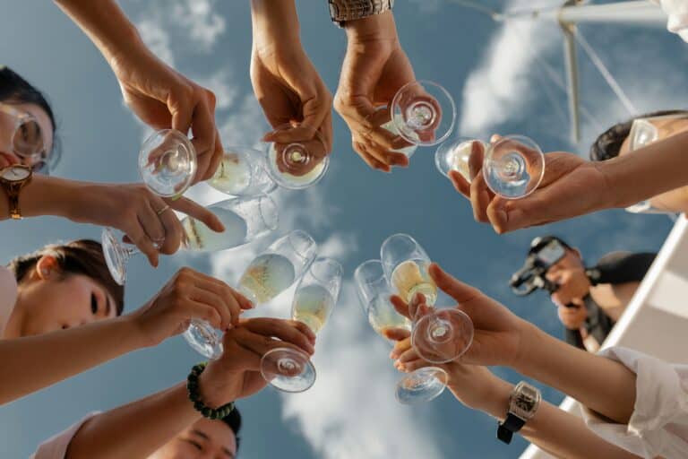 This image shows a group of people huddled in a circle, lifting their glasses up to cheers. Their glasses contain alcoholic drinks. What Does the Bible Say About Alcohol?