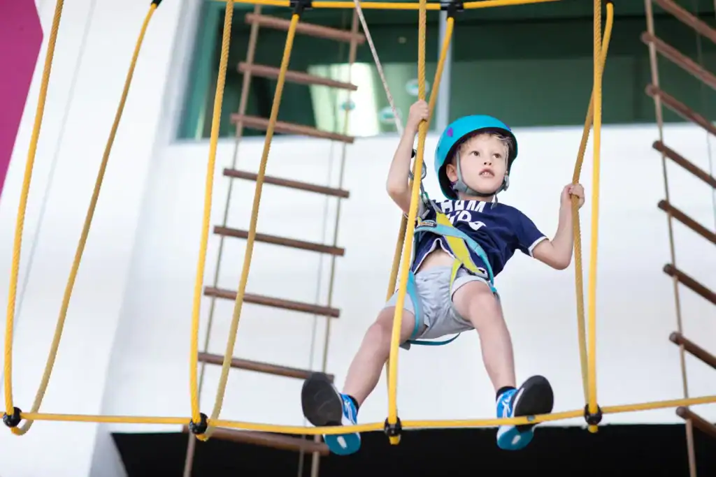 Young boy climbing a rope course in safety gear, representing the adventurous spirit involved in raising boys.