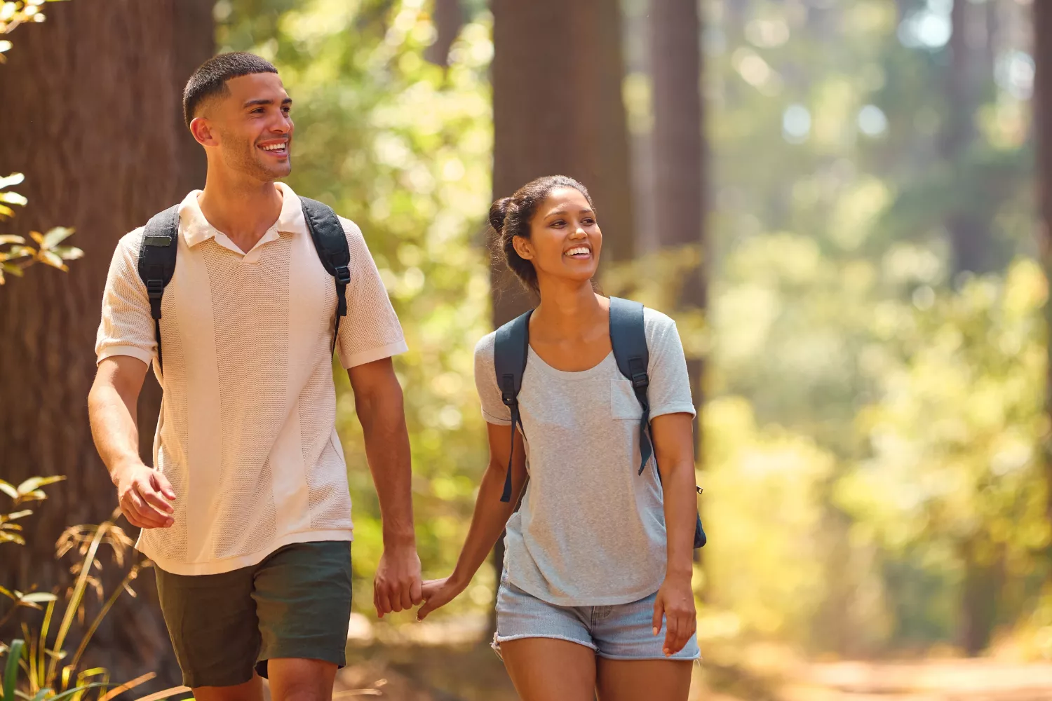 Smiling couple holding hands on a forest trail, symbolizing unity, trust, and biblical leadership in relationships.