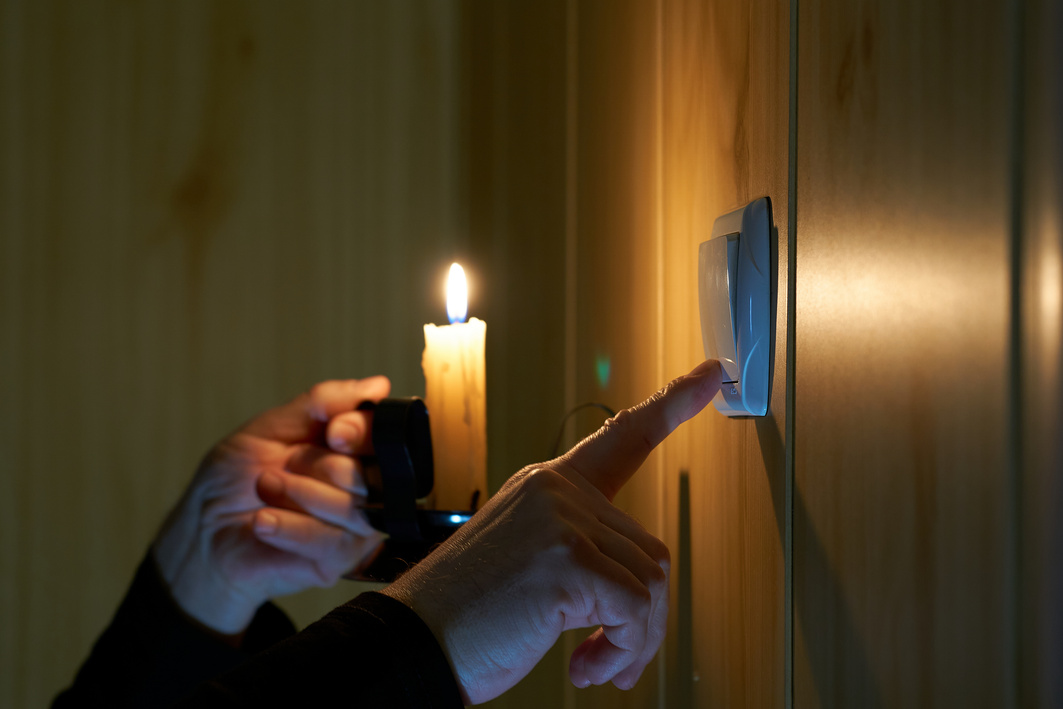 A man with a burning candle in his hand flips a light switch on and off.